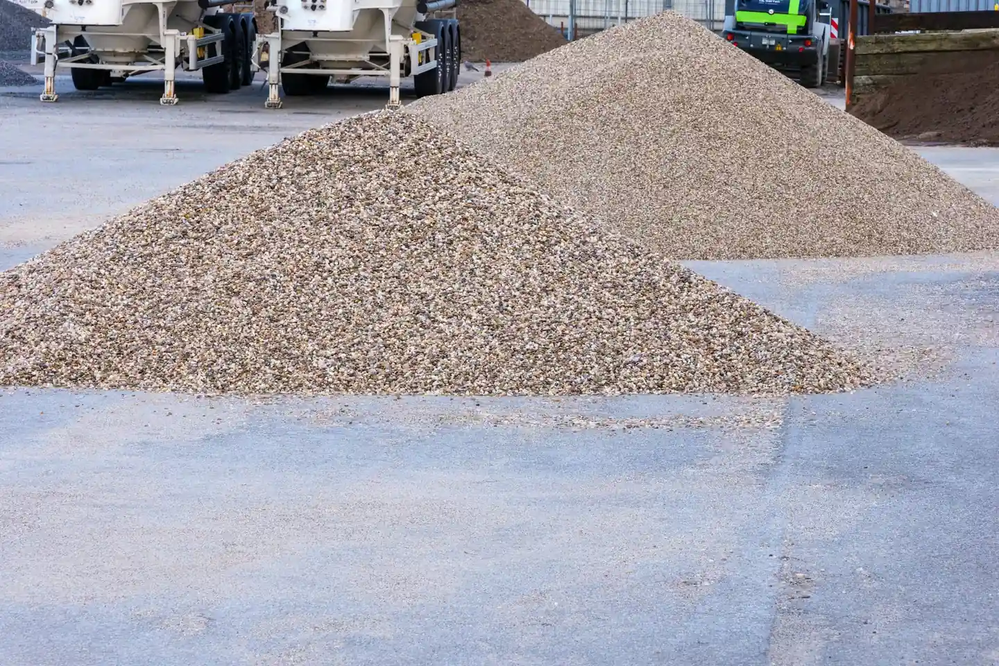 material being separated or loaded inside a fenced site, mid-shift, working light. Equipment in frame with the ground it is moving. Wide, horizon low, machine in the lower third.