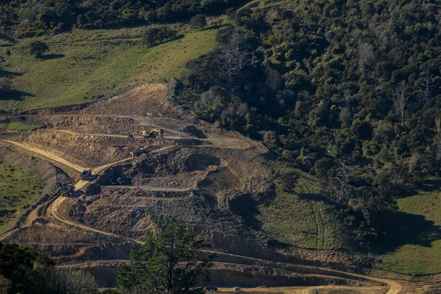 grading and earthwork in progress — the ground being changed. Access roads or pad construction mid-build, at distance, in its setting.